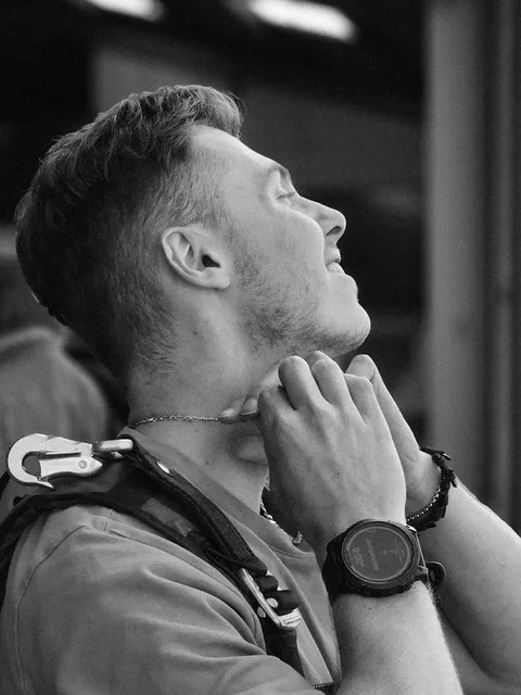Esteban Thilliez in a skydiving harness, looking up, in black and white.
